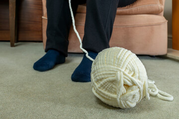 Ball of chunky chenille crochet yarn with yarn on carpet floor and leading up out of frame to woman...