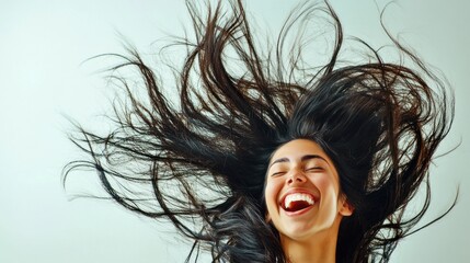 Fototapeta premium A young woman bursts into laughter, her long hair soaring around her as she expresses joy. The soft background highlights her vibrant energy, capturing a moment of pure happiness