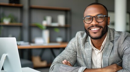 A confident man with glasses smiles while seated at his desk in a contemporary office. Natural light floods the room, enhancing the modern decor and atmosphere