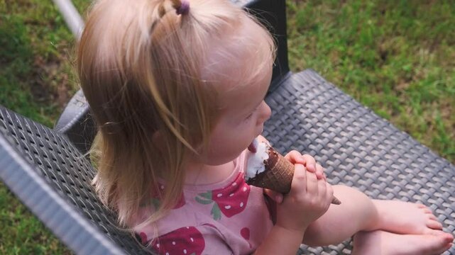 Cute caucasian little child 2 years girl licks an ice cream cone in the summer outside.