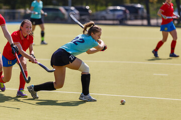 Female attacker hitting the ball in an intense field hockey match on a sunny afternoon