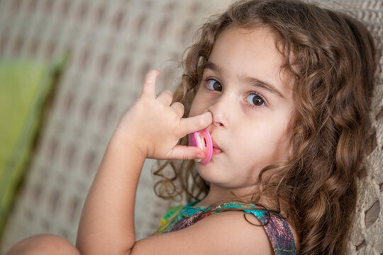Uma menina chupando chupeta e cutucando o nariz.