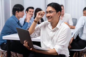 Confidence and happy smiling businessman portrait with background of his colleague and business team working in office. Office worker teamwork and positive workplace concept. Prudent