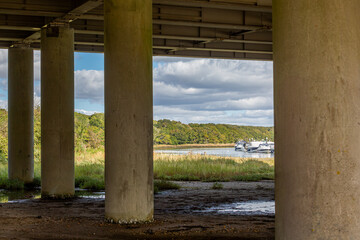 River Hamble from underneath the M27 bridge on a autumn's day, Image shows beautiful landscaped wooded country park and moored boats on a calm day through the M27 bridge concrete beam supports