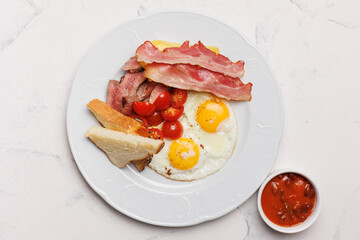Hearty breakfast with bacon, fried eggs, fries and vegetables.