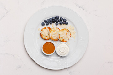 Appetizing cheese pancakes with blueberries and honey on a large white plate