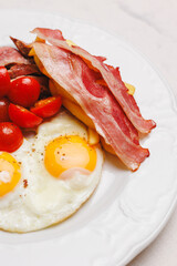 Hearty breakfast with bacon, fried eggs, fries and vegetables.