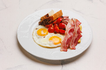Hearty breakfast with bacon, fried eggs, fries and vegetables.