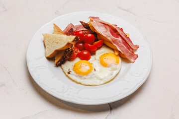 Hearty breakfast with bacon, fried eggs, fries and vegetables.
