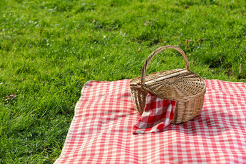 One picnic wicker basket with checkered napkin and blanket on green grass. Space for text