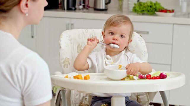 Little toddler eating soup using spoon, learning how to feed himself. Baby lead weaning