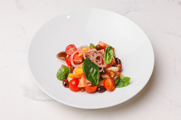 Appetizing salad with tomatoes, onions, olives and crispy croutons in a large white plate.
