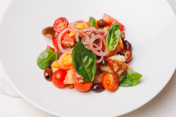 Appetizing salad with tomatoes, onions, olives and crispy croutons in a large white plate.