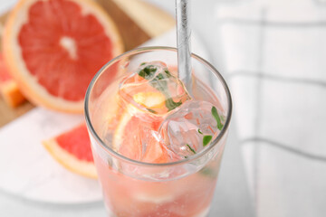 Refreshing water with grapefruit and rosemary in glass on light table, closeup