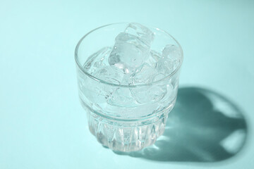 Refreshing water with ice in glass on turquoise background, closeup