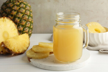 Tasty pineapple juice in mason jar and fresh fruits on white wooden table against grey background, closeup