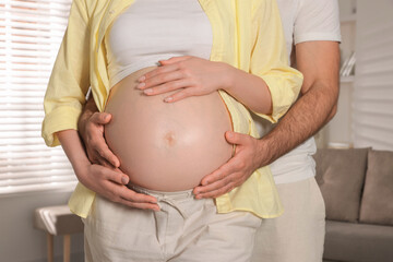 Man touching his pregnant wife's belly indoors, closeup