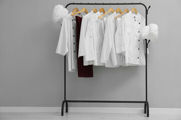 Chefs' uniforms on clothing rack near grey wall indoors. Space for text