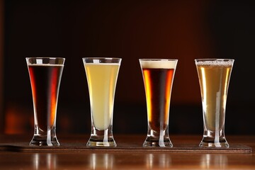 Glasses with different types of beer on wooden table against color background