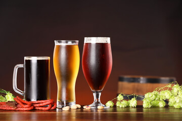 Glasses with different types of beer, snacks and fresh hops on wooden table in bar