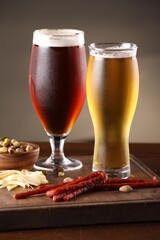 Glasses with different types of beer and snacks on wooden table, closeup