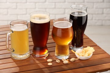 Glasses with different types of beer and snacks on wooden table against white brick wall