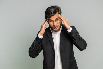 Displeased exhausted Indian business man rubbing temples to cure headache problem, suffering from tension, migraine, stress, grimacing in pain, high blood pressure isolated alone on gray background