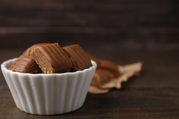 Tasty sweet caramel candies in bowl on wooden table, space for text