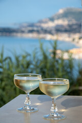 Sparkling wine, cava or champagne in two coupe glasses on table with view on blue sea, Menton and Monte-Carlo, French Riviera, France is summer