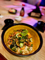 Traditional japanese food in a bowl on a wooden table. Rice with vegetables, seafood and sesame seeds in a bowl with chopsticks