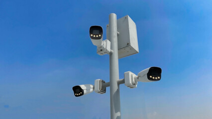 A tall surveillance pole with four cameras and a control box stands against a clear blue sky, ensuring wide-area monitoring.