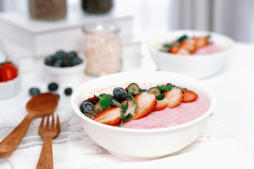 Presented by fruits putting yogurt toppings with strawberry, berry, oats, raisins and chia seed decorated by peppermint in white blow. Pink background. Set of healthy dairy product choice. Pecuniary.