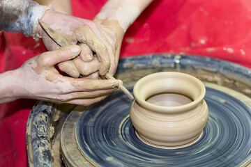 Two pairs of hands mold something from clay on a potter's wheel