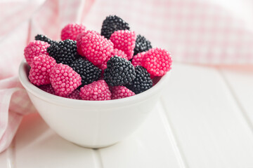 Sweet jelly candies in bowl on white table.