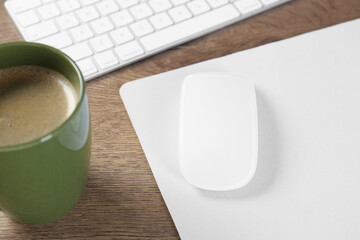 Computer mouse with mousepad, keyboard and cup of coffee on wooden table