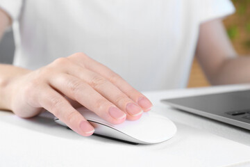 Fototapeta premium Woman using computer mouse while working with laptop at white table, closeup