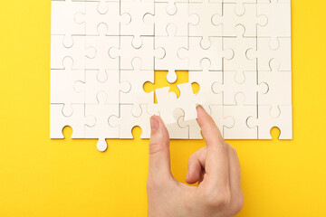 Woman solving white puzzle on yellow background, closeup