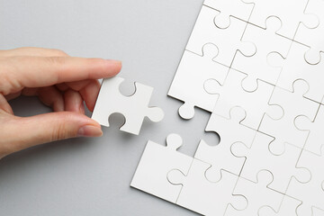 Woman solving white puzzle on light grey background, top view