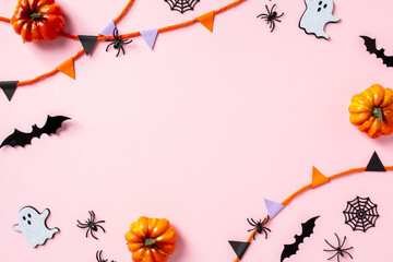Halloween frame of pumpkins, ghost, bats, spiders, and garland on pastel pink background. Flat lay, top view, copy space.