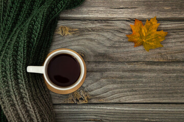 Overhead Autumn Composition. Mug of Tea, Green and Grey Knitted Scarf, Autumn Leaf on Wooden Background.