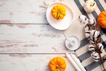 Autumn flat lay with orange pumpkins, white candles, cotton branches, and a striped cloth on a wooden surface. Ideal for seasonal decor, Thanksgiving, and fall-themed promotions