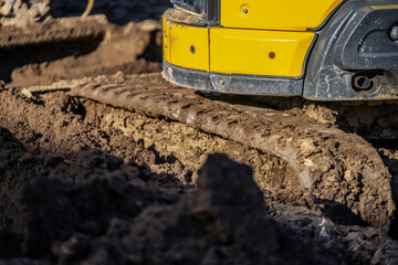 Yellow mini excavator rubber tracks very deep in the construction yard mud at least 5 inches deep