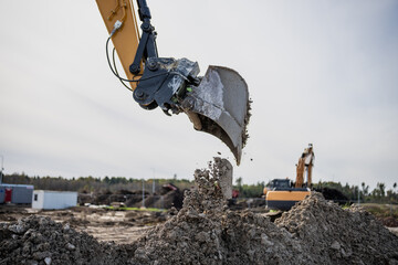 Large excavator arm working on construction yard excavating gravel, rocks, earth. Construction earthmoving business operator operating on earth restructurization