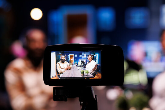 Focus on vlogging camera used by cohosts in blurry background streaming podcast during live debate on vlog channel. Close up of professional recording gear used by man and woman in studio to film show