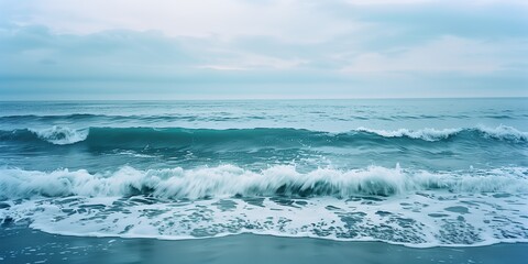 Fototapeta premium Soft ocean waves caressing the sandy shore on a quiet summer day with a calm, overcast sky