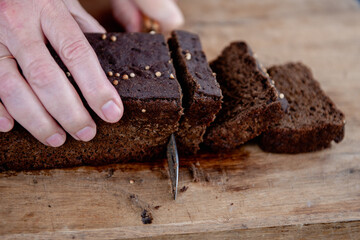 The man cuts whole-wheat rye bread on a wooden cutting board.