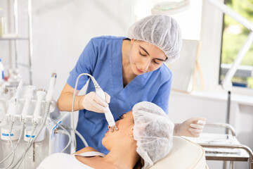 Obraz premium Young woman cosmetologist performs hardware facial microcurrent procedure to young female patient