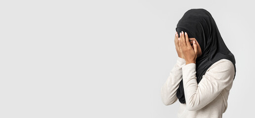 Violence against muslims concept. Upset black woman in hijab covering face with hands, crying over...