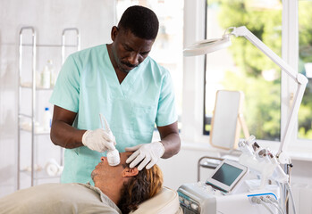 Male cosmetologist performs skin care and maintenance procedure for man client. Specialist uses...