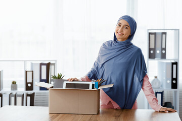 Promotion Concept. Smiling Muslim Female Office Employee Standing Near Desk With Box Full Of Her...